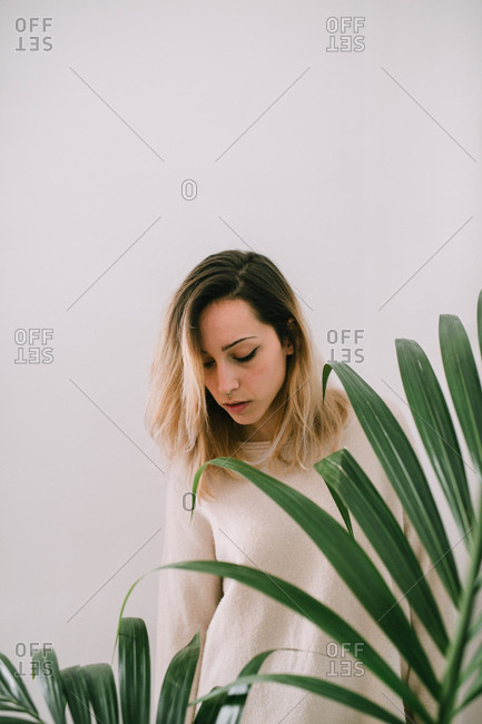 Young sleepy woman standing near the plant. Vertical indoors shot.