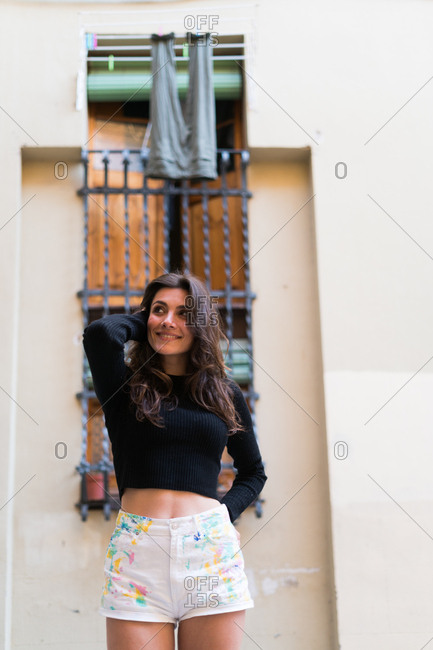 Young smiling woman wearing trendy outfit and posing on ground near fence while smiling at camera.