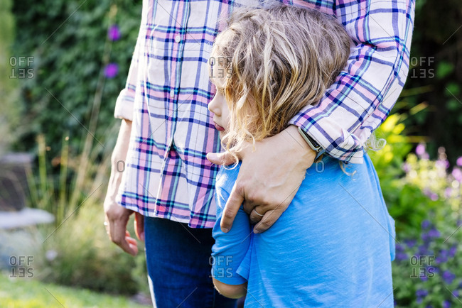 Midsection of mother standing with son in yard during sunny day