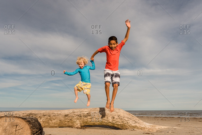 Two brothers leaping from driftwood on a beach