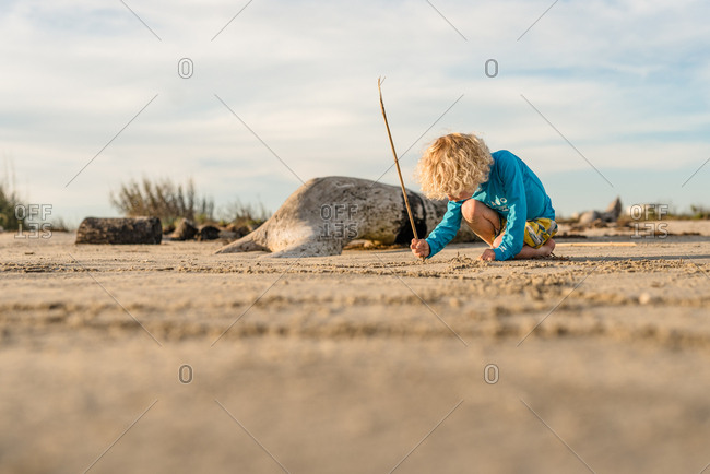 Boy drawing in sand with a stick