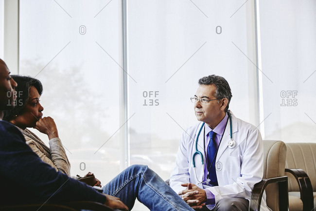 Confident mature male doctor discussing with mother and son in waiting room