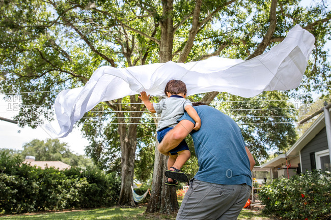 Father and son running through sheets drying on a clothesline