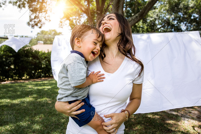 Mother and son laugh as they run through sheets on clothes line