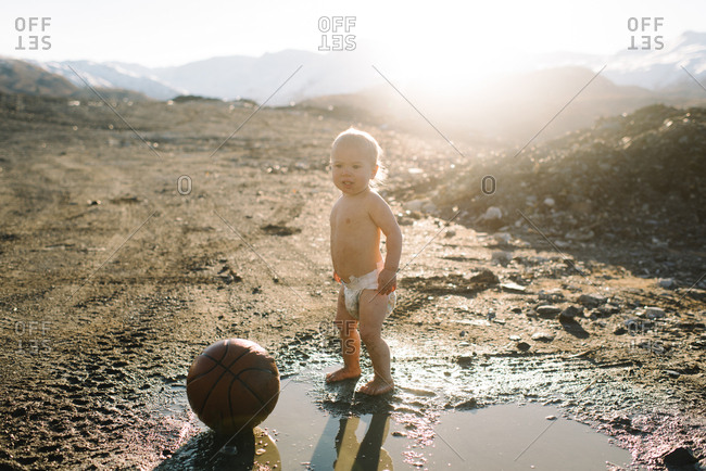 Baby in diaper with ball in mud puddle