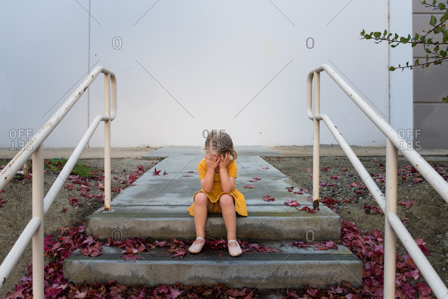 Little girl sitting on steps covered with leaves covering her face