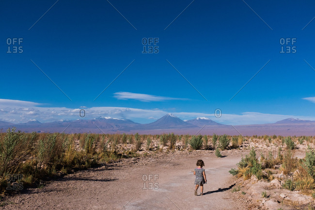 Young girl walking along a path through the desert with mountains in the distance