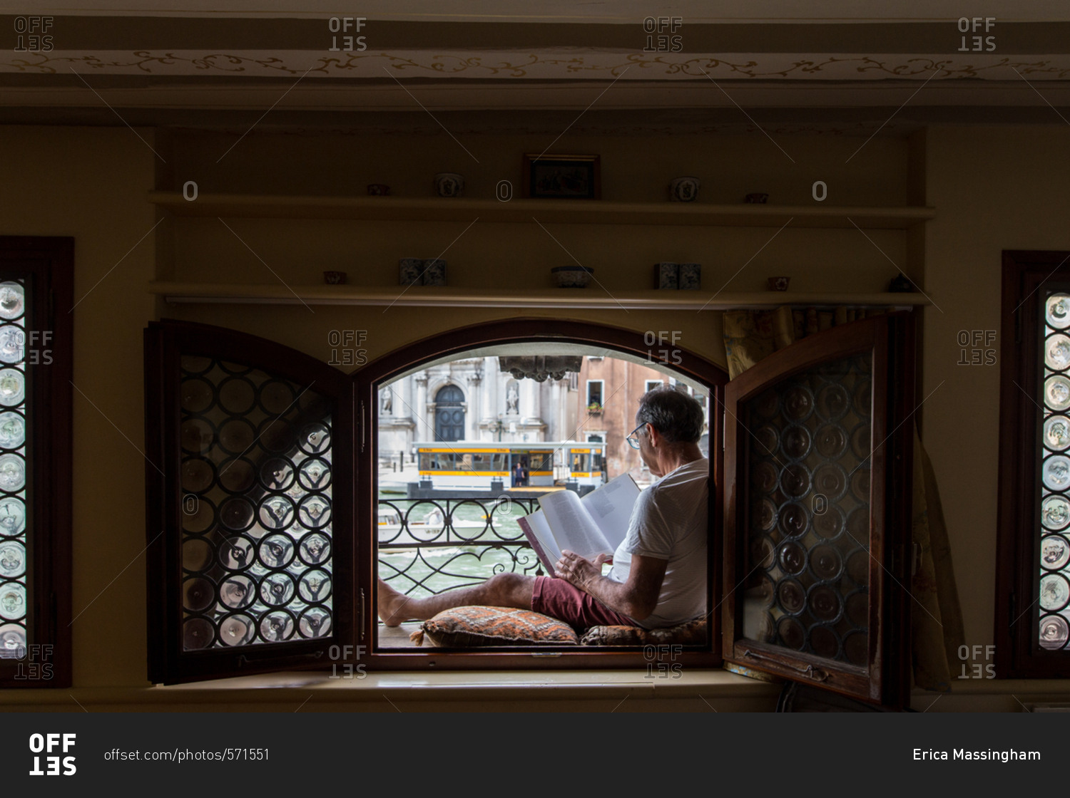 A man reading in his window seat, looking out to the Grand Canal