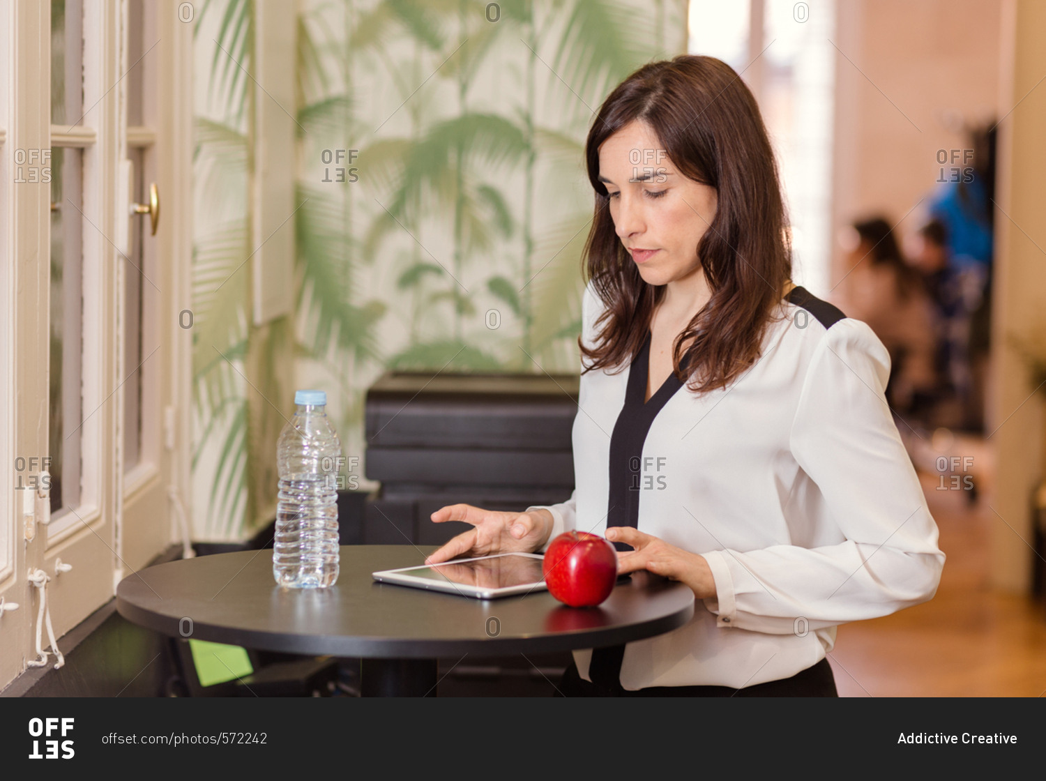 Front view of young beautiful female in blouse sitting and using tablet at the table.