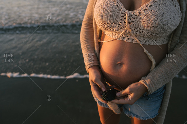 Pregnant woman holding seashell on beach