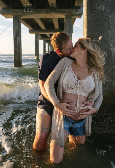 Man kissing pregnant woman under pier