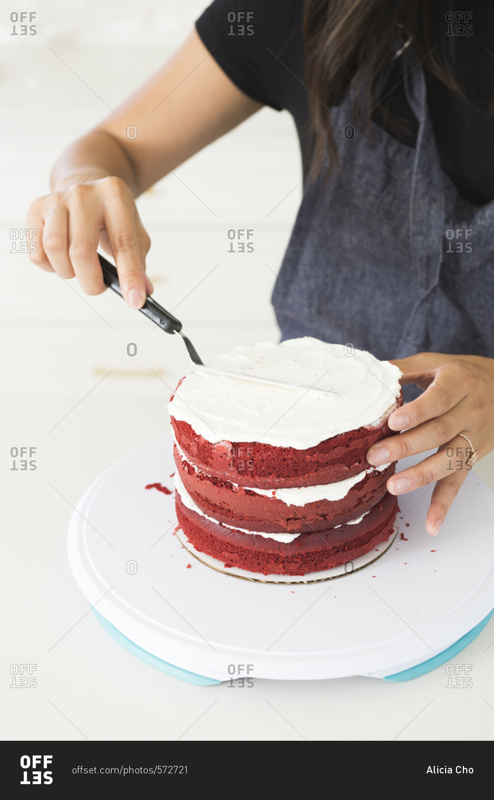 Baker frosting a red velvet cake with white icing