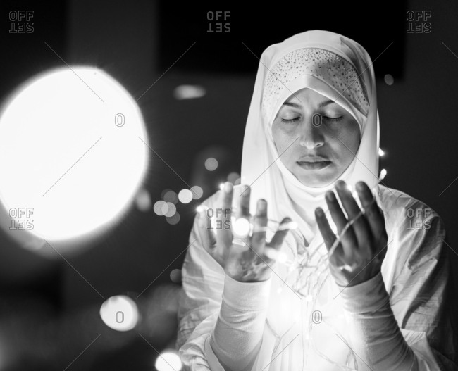 Muslim woman praying in dark room with nice lights around her