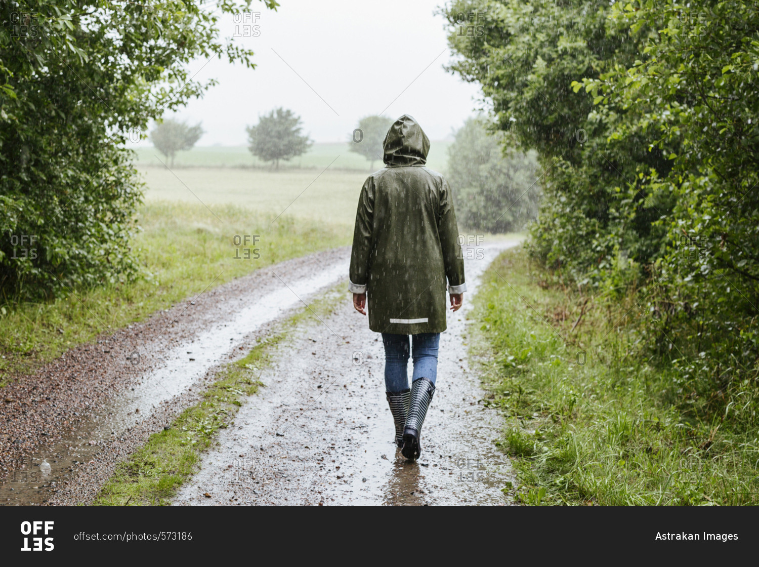 Rear view of woman in green raincoat walking in rain