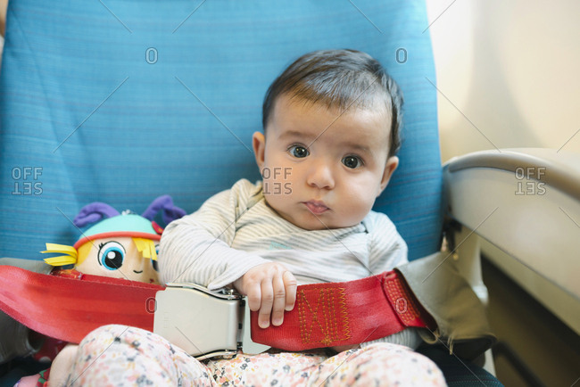 Baby girl sitting on a plane seat with a doll and the seat belt fastened