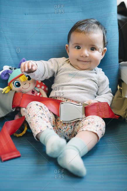 Happy baby girl sitting on a plane seat with a doll and the seat belt fastened