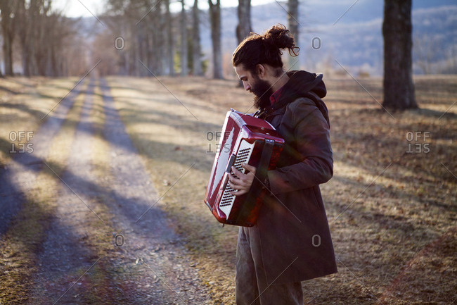 Side view of male hipster playing accordion at field during vacation