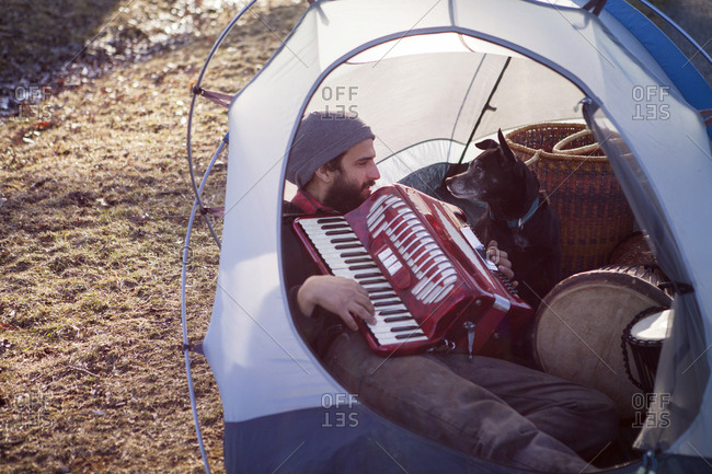 Man playing accordion for dog while sitting in tent at campsite