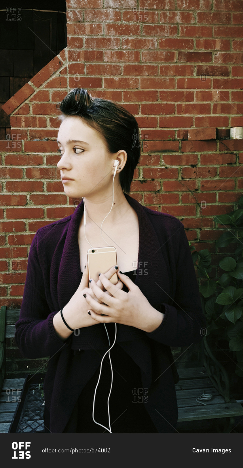Teenage girl listening music while standing against brick wall in backyard