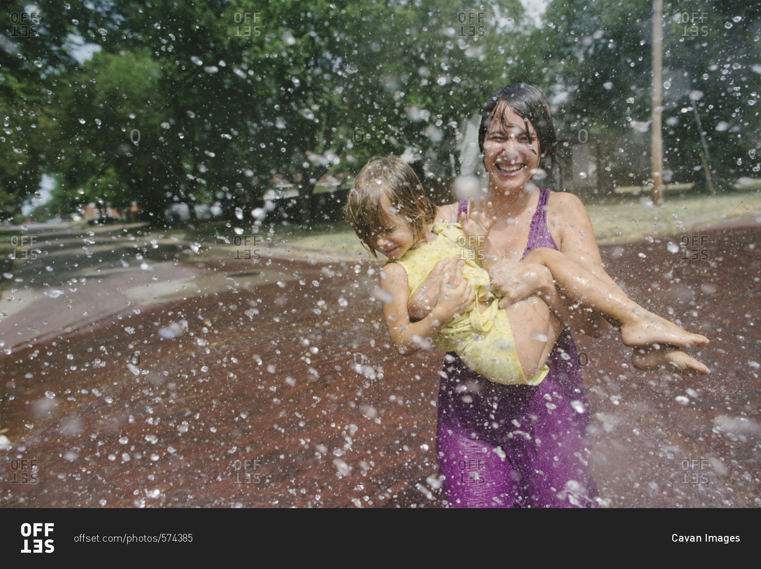 Playful mother carrying daughter while enjoying in fountain at park