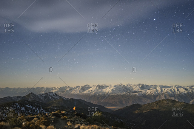 Distant view of hiker standing amidst mountains against star field sky