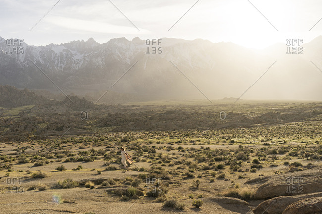 Distant view of young woman walking on field against mountains