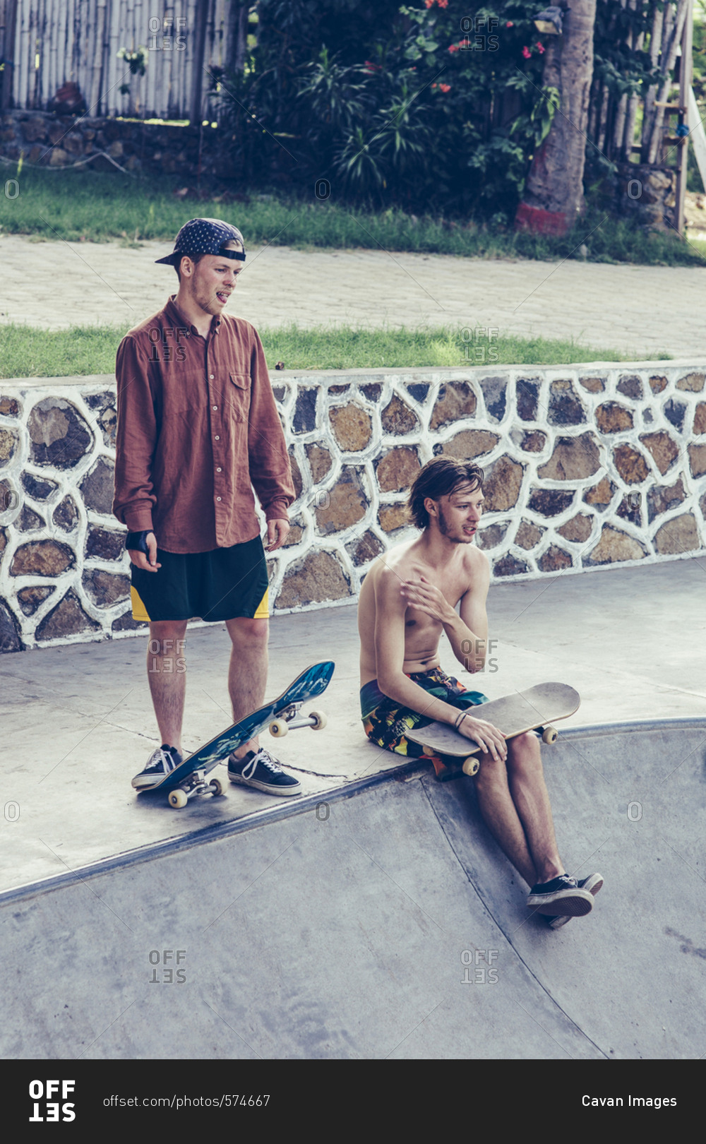 Young male friends resting with skateboards at the edge of concrete pool
