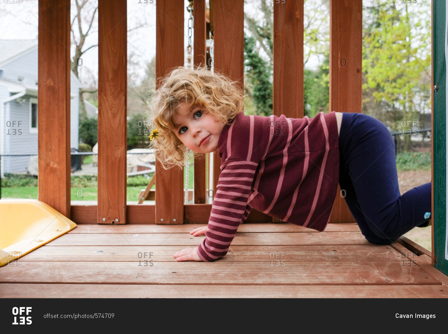 Side view portrait of girl kneeling on wooden outdoor play equipment at yard