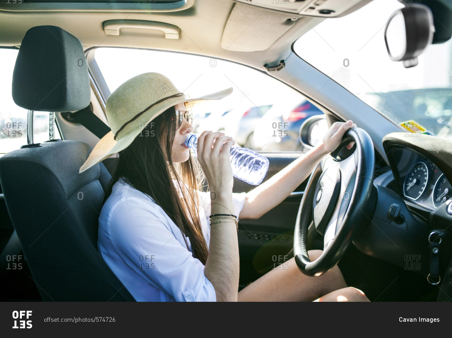Side view of young woman drinking water while sitting in car