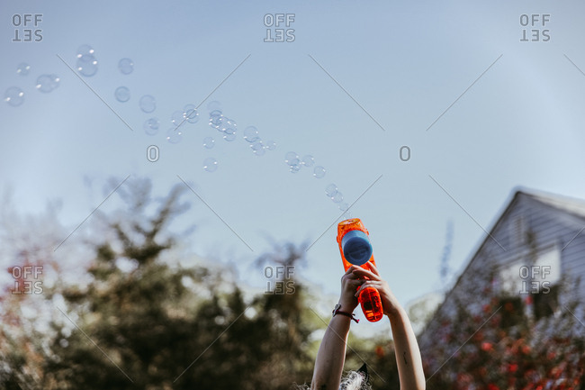 Cropped hands of girl playing with bubble gun at yard against clear sky