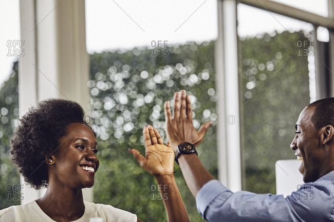 Happy male and female business colleagues giving high-five to each other at desk in office