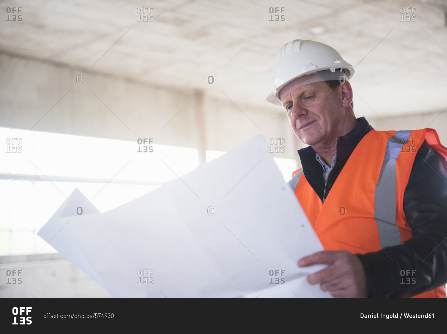 Man with plan wearing safety vest in building under construction