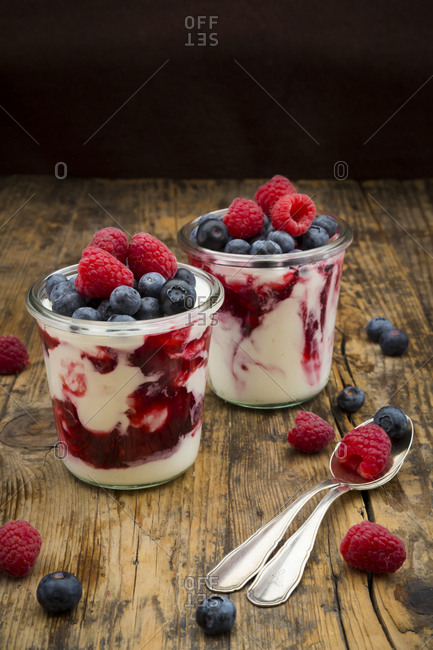 Two glasses of Greek yogurt with berry groats- fresh blueberries and raspberries on wood