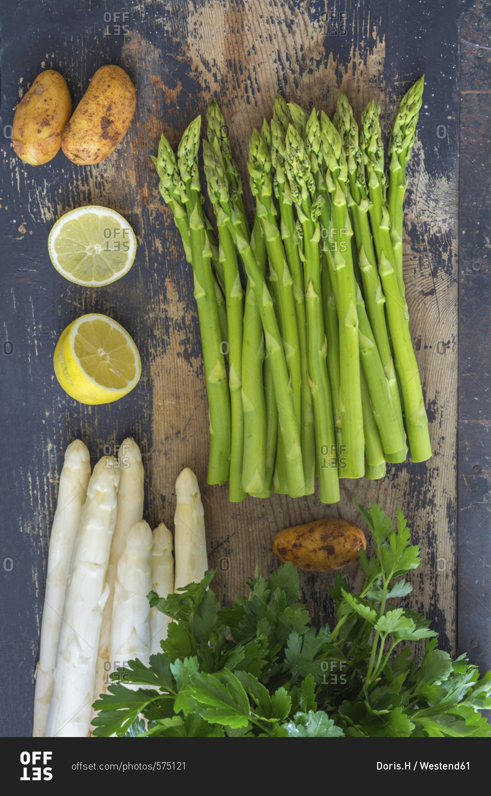 Green and white asparagus- potatoes- sliced lemon and flat leaf parsley on wood