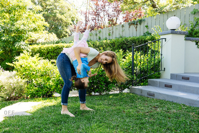 Full length of playful woman carrying daughter upside down at yard