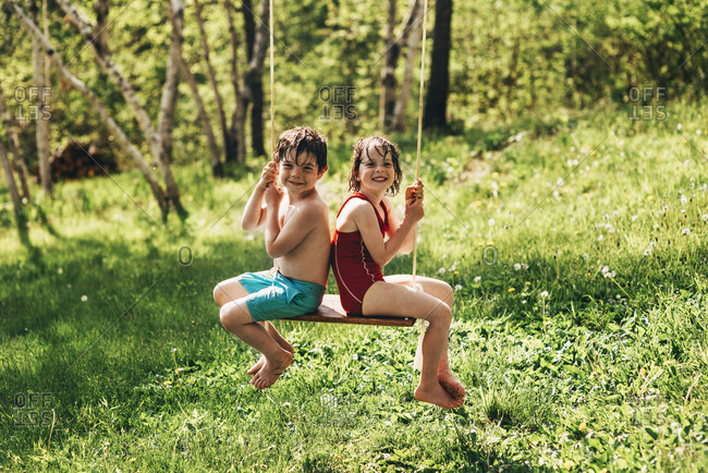 Young boy and girl swinging on a swing together in the summer