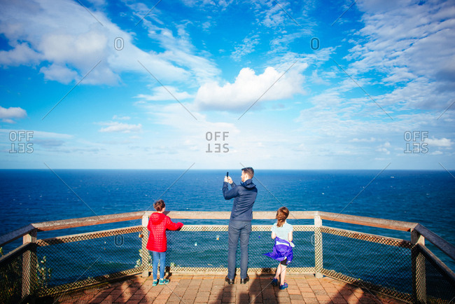 Father and daughters overlooking blue ocean and cloudy sky