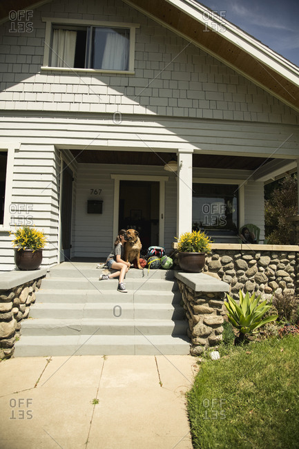 Girl sitting with dog on front steps of house