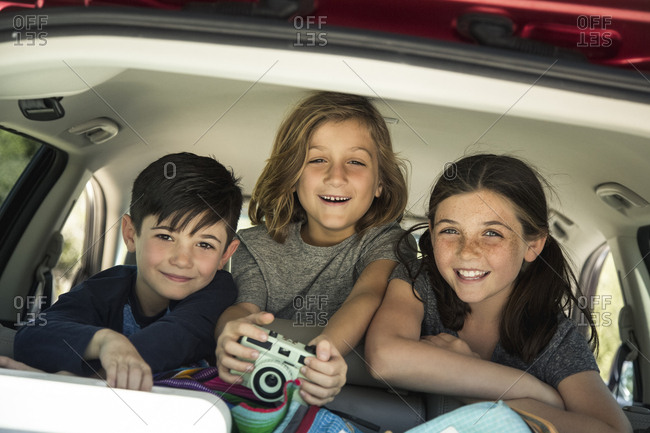 Portrait of happy siblings with camera in back seat of car