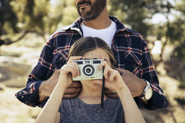 Girl photographing through vintage camera while standing with father in forest