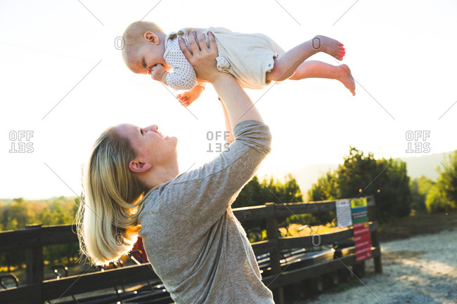 Woman lifting baby in the air outside on a sunny day