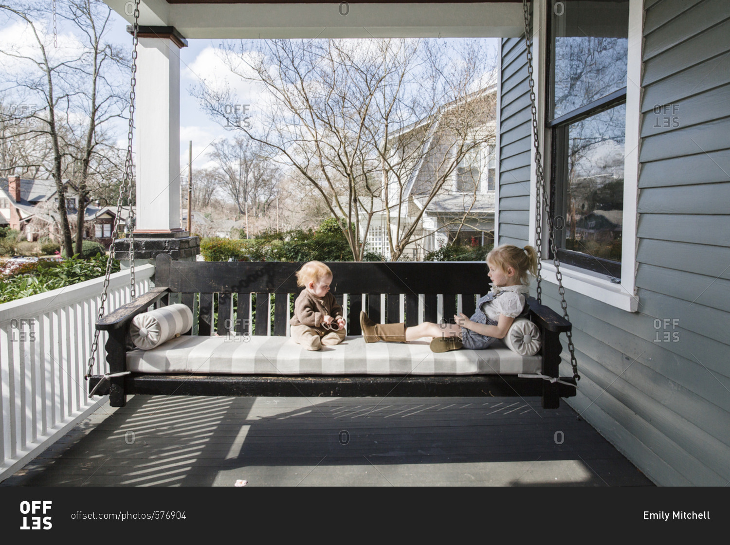 Two little girls sitting on front porch swing stock photo OFFSET