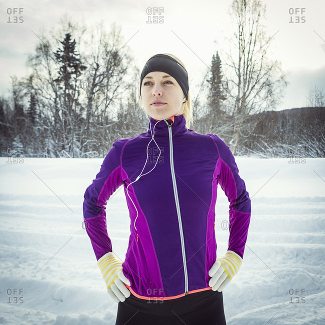 Adult female runner listening to music while warming up for her run on snow covered road.