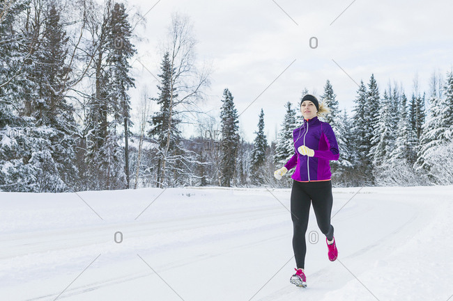 Portrait of adult female runner with her ear bugs after her run on snow covered road.