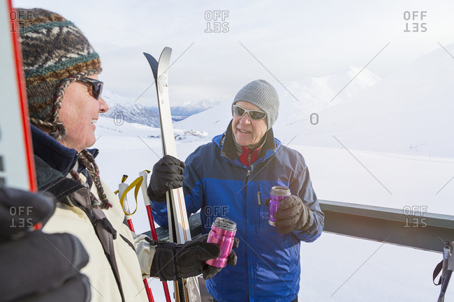 Two mature adult men relaxing on a deck, drinking soda, while taking a break from cross country skiing
