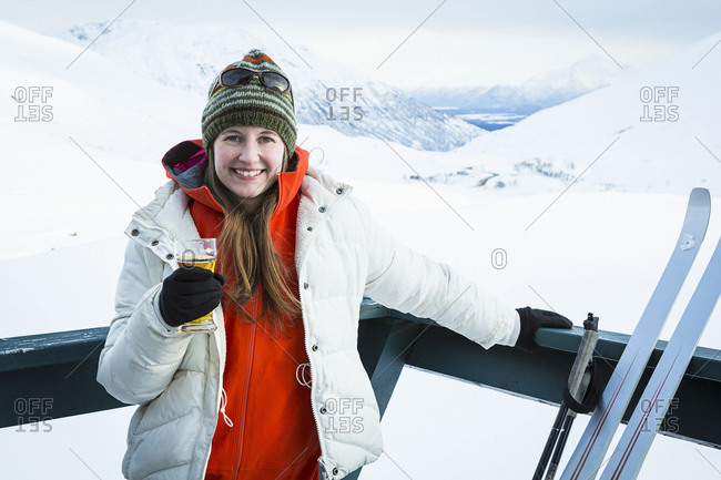 Young adult woman relaxing on a deck, having a beer while taking a break from cross country skiing