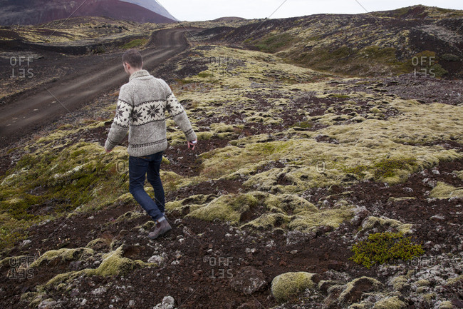 Man walking down a mossy lava field toward dirt road in Iceland.