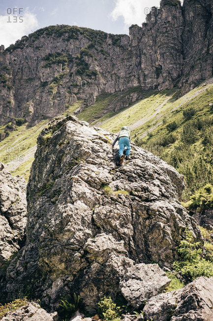 6 year old boy in blue pants climbing large boulder in alpine landscape.