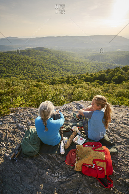 An older woman and a younger woman sitting together on a scenic rocky outcropping and having a snack during a backpacking trip together.