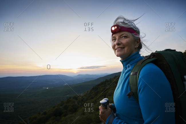 An older woman wearing a headlamp on a scenic rocky outcropping at dusk while on a backpacking trip.